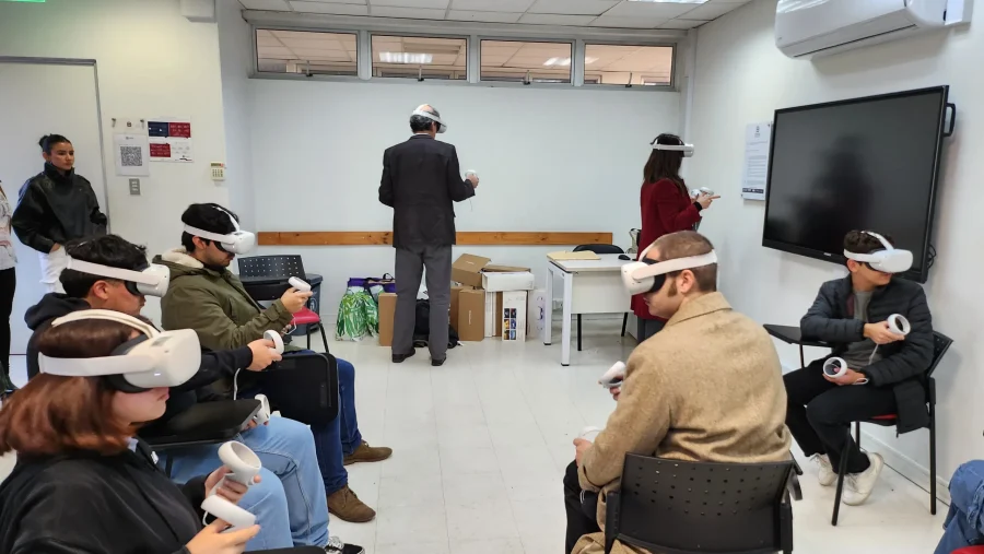 Group of adults seated in a bright room wearing VR headsets and using handheld controllers during a training session as an instructor or facilitator moves about at the front.
