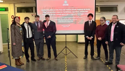 Eight people in business attire posing in a hallway, with a red presentation slide projected behind them.