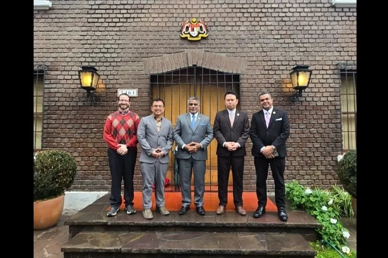 Five men in suits posing on steps outside a brick building with a crest above the door.