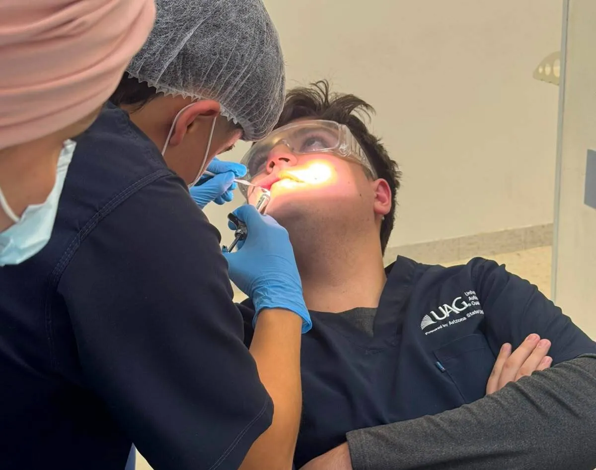 Dentist in scrubs and gloves performs a dental procedure on a patient wearing protective goggles.