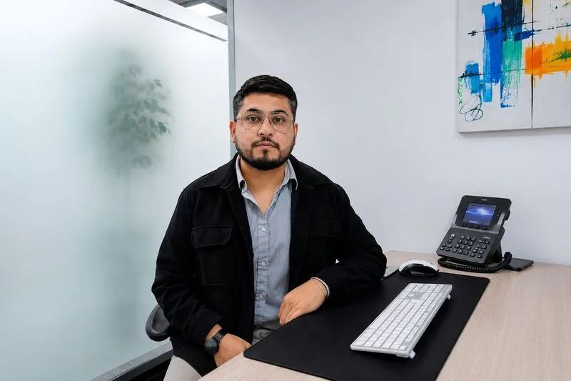 Professional man seated at an office desk with a keyboard, phone, and abstract wall art in the background