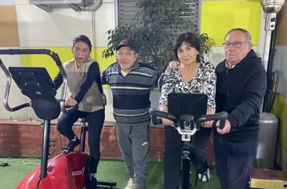 Four seniors stand beside stationary bikes in a gym, posing for a photo with smiles on their faces.