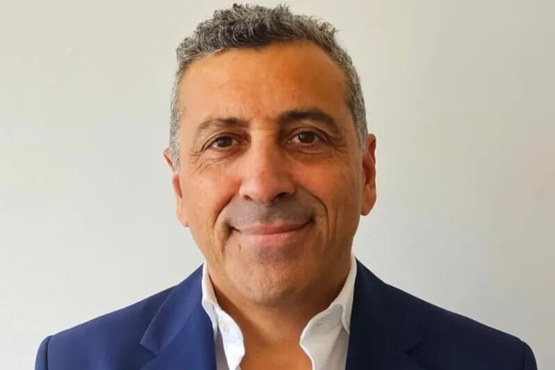 Smiling man in a navy blazer and white shirt, posed against a light neutral background (professional headshot).