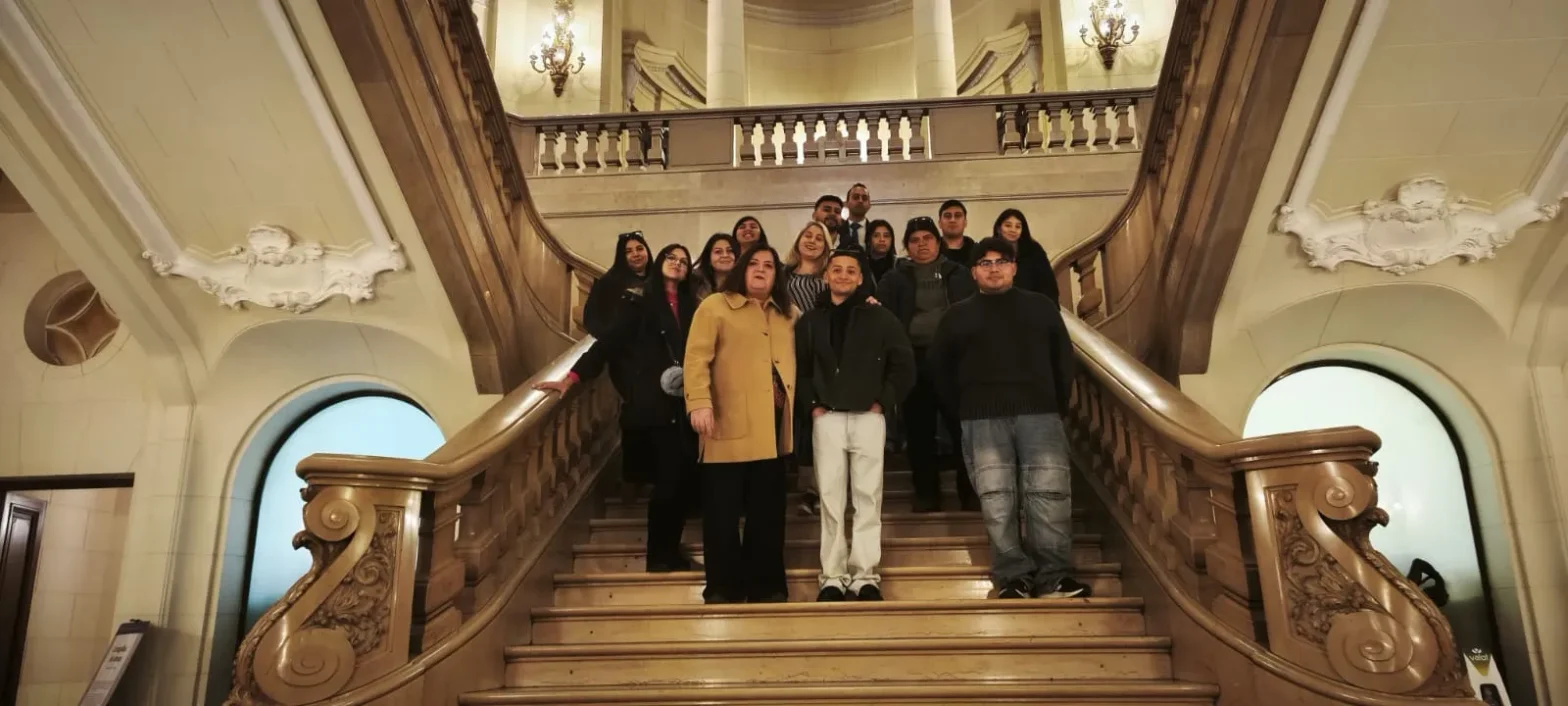 Group of people posing on a grand marble staircase inside a historic building, facing the camera, with ornate railings and arches in the background.