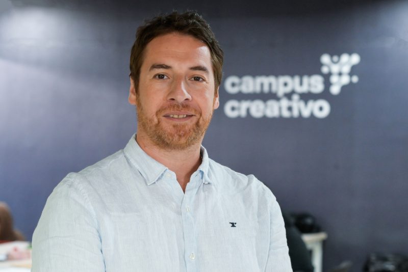 Portrait of a smiling man in a light blue button-down shirt, with a 'campus creativo' sign in the background.