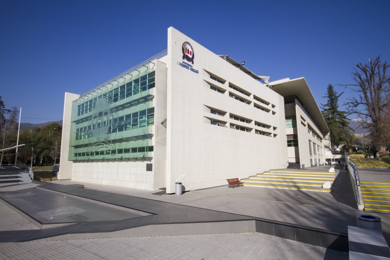 White modern university building with a glass façade, set under a clear blue sky and yellow entry stairs.