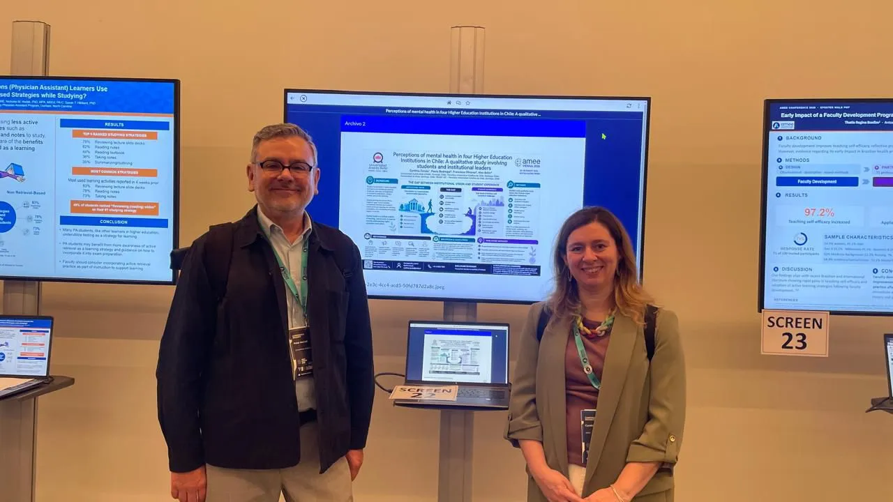 Two presenters stand in front of multiple large display screens showing research posters, at a conference booth with a laptop on a stand labeled SCREEN 23 nearby.